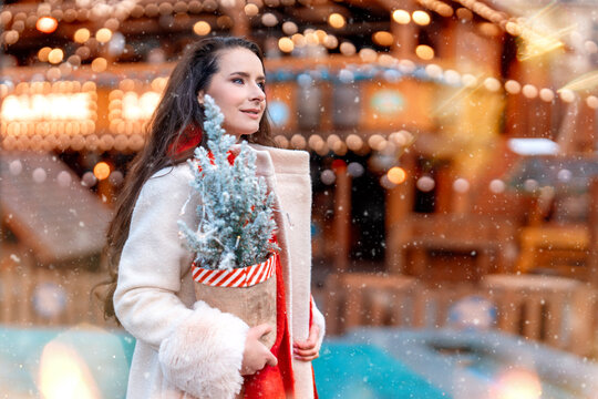 Elegant woman holding festive decorations while enjoying a winter wonderland at a Christmas market in the evening with string lights - Powered by Adobe