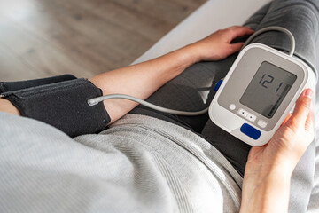 A person checks their blood pressure using a digital monitor while sitting indoors, highlighting a...