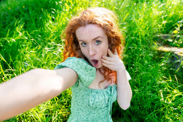 Young woman takes a playful selfie in a lush green field during daytime, showcasing her vibrant...