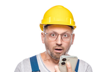 Scared middle-aged construction worker with mobile phone, isolated on white background. Shocked repairman holding smartphone. Unbelievable. Craftsman against white wall