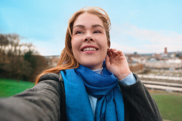 Smiling woman takes a selfie outdoors with a scenic view in the background during a bright and...