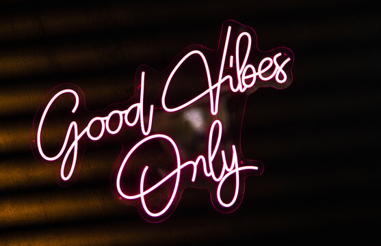 Pink neon sign promoting good vibes only on dark background