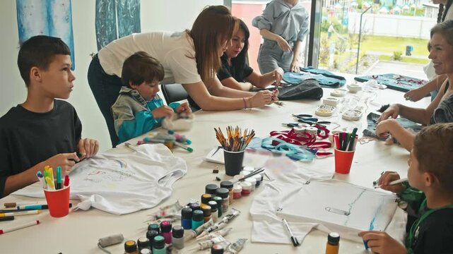 Group of parents, together with their children, create unique craft items of clothing. They decorate them and create beautiful drawings.