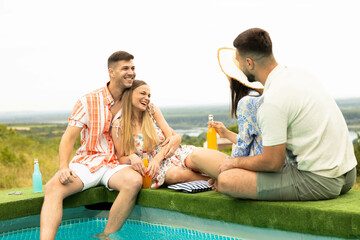 A group of four friends celebrates summer by the pool, laughing, enjoying drinks, and making happy memories outdoors.