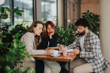 Three professionals discussing business strategies at a stylish cafe, fostering teamwork and productivity in a refreshing ambiance with greenery.
