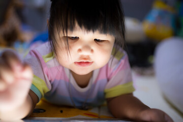 A little Asian girl is lying on the bed watching a tablet,Asian girl lying on bed in bedroom and looking at tablet screen alone with happy moment. Concept of internet, social media.