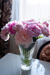 Beautiful peonies in a glass vase in bright sunlight.