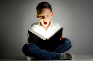 Curious young boy looking amazed while reading an open book, reacting with wide eyes to the content.