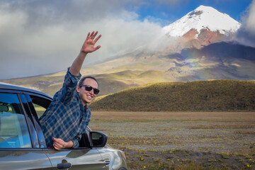 Joyful traveler leans out of a car window, waving enthusiastically with a stunning snow-capped...
