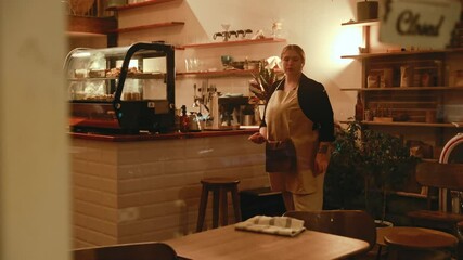 The female owner carries a laptop from the table to the bar counter and wipes the tables with a male employee