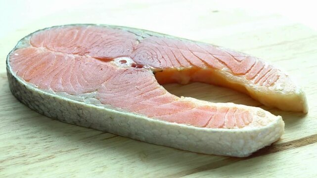 A raw salmon steak on a wooden board shows its natural texture