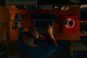 Portrait of a young caucasian man wearing wireless headphones using a laptop sitting in a cosy...