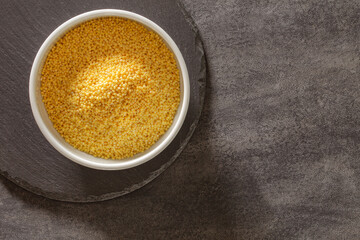 millet groats in bowl on dark countertop, top view