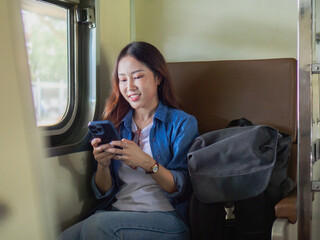 A young woman sits on a train, pressing her phone.