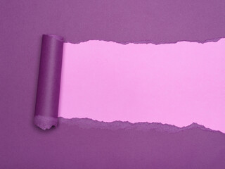 A piece of purple paper is torn to reveal a lighter pink layer underneath