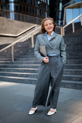 Confident professional poses on urban steps with laptop in hand during a sunny day