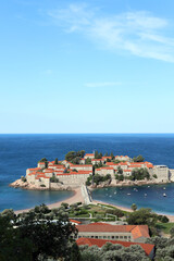 Scenic view of Sveti Stefan island, a luxury resort on the Adriatic coast of Montenegro, connected to the mainland by a narrow isthmus and surrounded by deep blue sea.