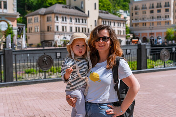 Family mother and little child 3 year in Rosa Khutor resort, buildings and river at the foot of the...