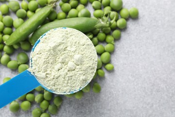 Protein powder in measuring spoon and fresh green peas on light grey table, flat lay. Space for text