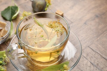 Fresh linden tea in cup, sugar cubes and flowers on wooden table, closeup. Space for text