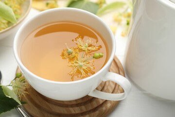 Fresh linden tea in cup and flowers on white wooden table, closeup