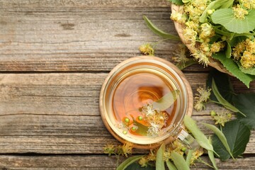 Tasty linden tea in cup, leaves and flowers on wooden table, flat lay. Space for text