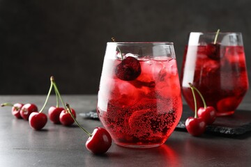 Tasty cherry soda with ice cubes and berries in glasses on grey table, closeup
