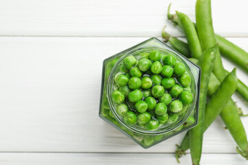 Fresh green peas in pickling jar and pods on white wooden table, flat lay. Space for text