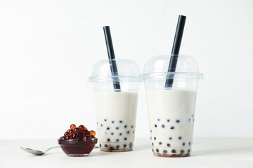 Tasty milk bubble tea in plastic cups and tapioca pearls on white table