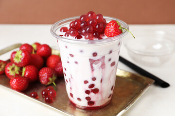 Tasty milk bubble tea in plastic cup and strawberries on white table, closeup