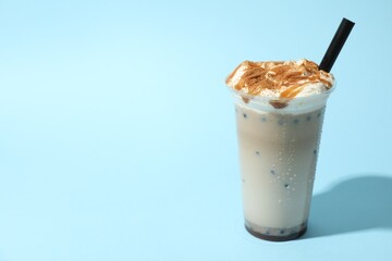 Tasty milk bubble tea in plastic cup on light blue background, space for text
