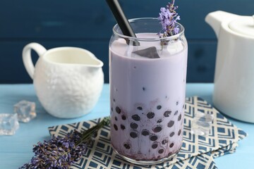 Tasty milk bubble tea in glass and lavender flowers on light blue wooden table, closeup