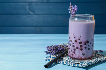 Tasty milk bubble tea in glass and lavender flowers on light blue wooden table, closeup. Space for...
