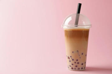Tasty milk bubble tea in plastic cup on pink background. Space for text