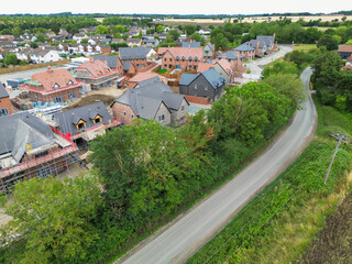 Aerial view of nearly completed, expensive and detached family homes seen on a housing development site in rural Essex, UK. A country lane snakes passed to the development to a nearby old village.