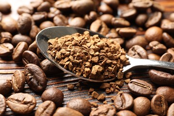 Spoon with instant coffee and beans on wooden table, closeup
