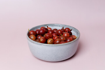 Fresh gooseberries with water drops in blue ceramic bowl, isolated on plain purple background, banner
