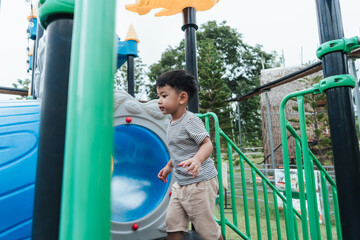 Asian boy playing on outdoor playground. Active child exploring and learning through physical play. Childhood development, self-esteem, motor skills and fun outdoor activity concept.