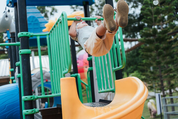 Asian boy hanging and swinging on playground bar, showing active energy and physical development....