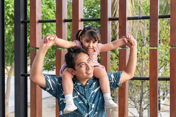 Obraz premium Hispanic father carrying daughter on shoulders, enjoying family time outdoors