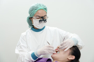 Asianfemaledentist using magnifying loupe examining teeth of adult female patient sitting on chair...