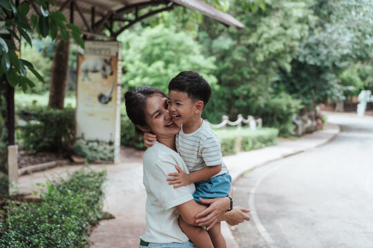 Happy Asian mother and son sharing a joyful laugh during a walk in a tropical zoo. The candid moment of affection and bonding captures the warmth of family time and carefree childhood.