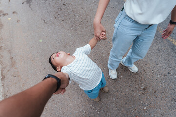 Asian toddler throwing a tantrum while holding hands with parents on a zoo outing. The child leans...