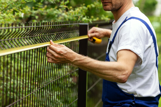 fencing services. worker taking measurements with measuring tape for new fence