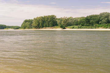 Danube river flowing gently with sandy banks and a dense forest line under a soft sky, creating a...