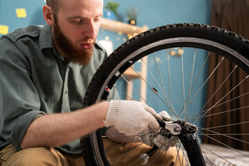 Portrait of Young bearded man fixing wheel with wrench while repairing bicycle at home