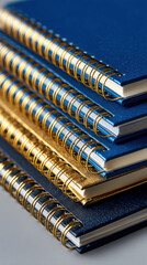 Pile of stylish blue and gold notebooks with spiral bindings, close-up angle, clean modern background