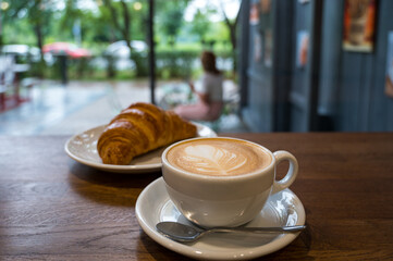 Warm cappuccino and fresh croissant served by the window in a cozy café, evoking a peaceful...