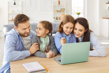 Positive family with children spending leisure time together, resting at home, enjoying online entertainment in internet using a laptop at the table. Bonding, relaxation, and digital activities.
