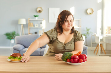 Plus size woman refusing eating hamburger as keeping to diet chooses plate with healthy vegetables...